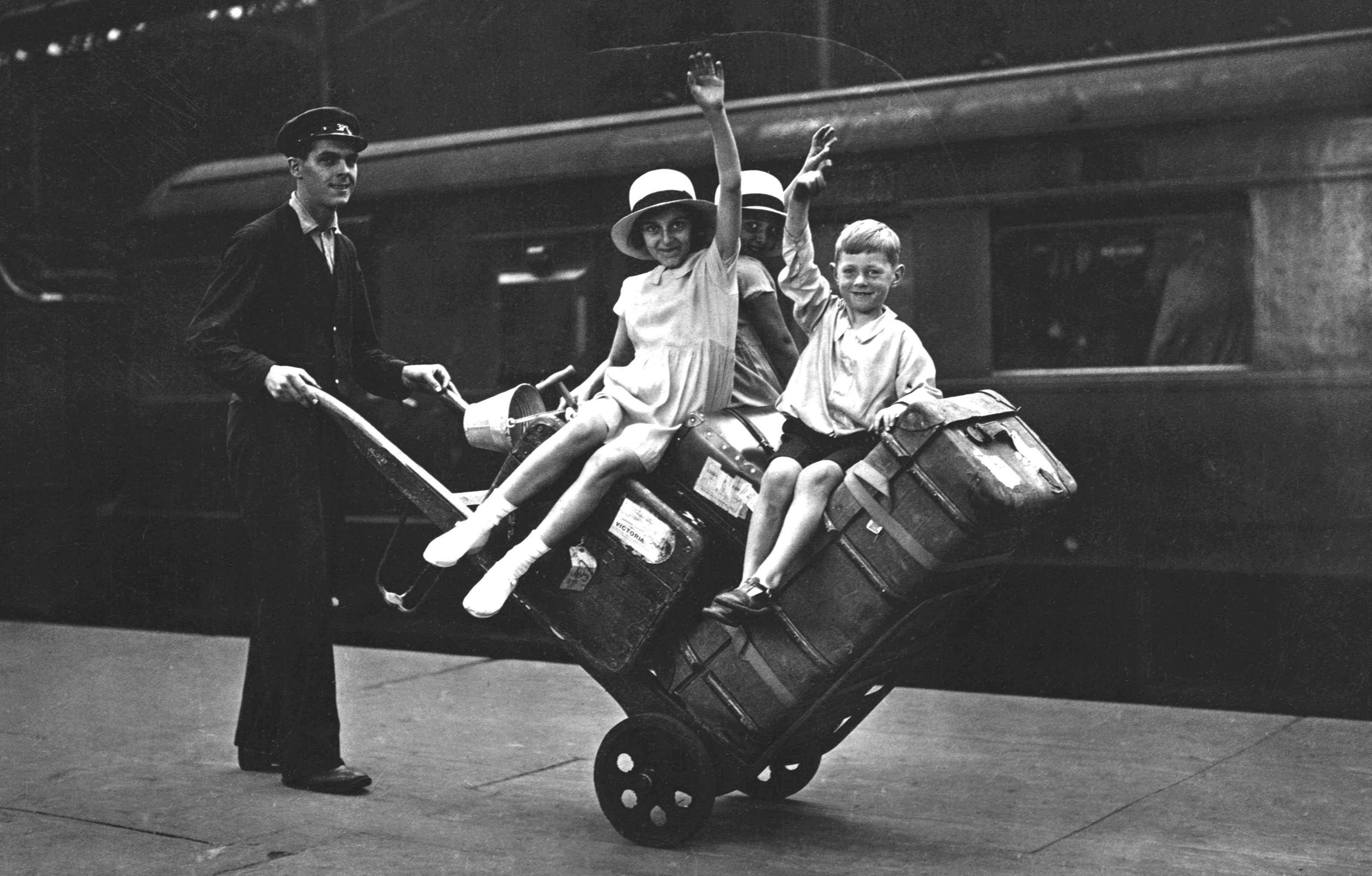 A porter pushes three children and their luggage on a trolley at a train station.