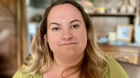 Nikki Fox/BBC Mary Hines standing in her kitchen in Norfolk. She has long blonde, wavy hair and a light green top on. She is looking directly at the camera with a neutral expression. 
