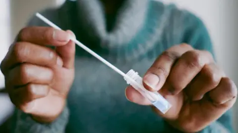 Getty Images Anonymous shot of a person wearing a green polo neck jumper and holding a plastic test tube and a pipette. 