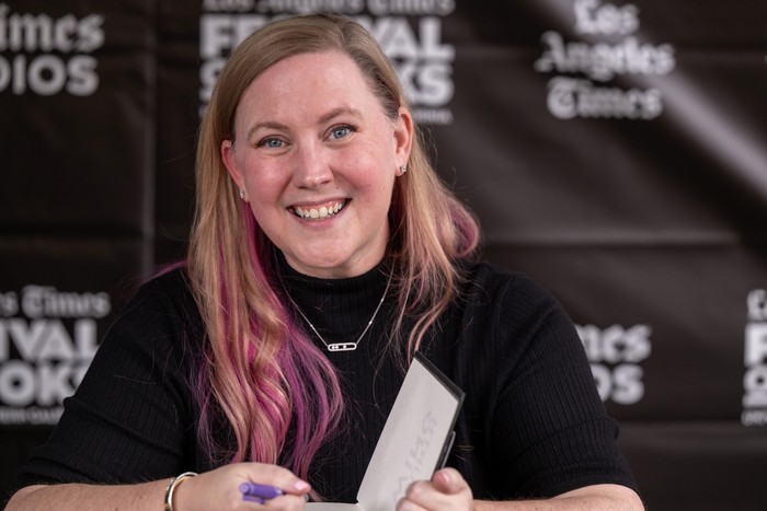 Rebecca Yarros smiling while sitting down at a book signing and holding the front page open.
