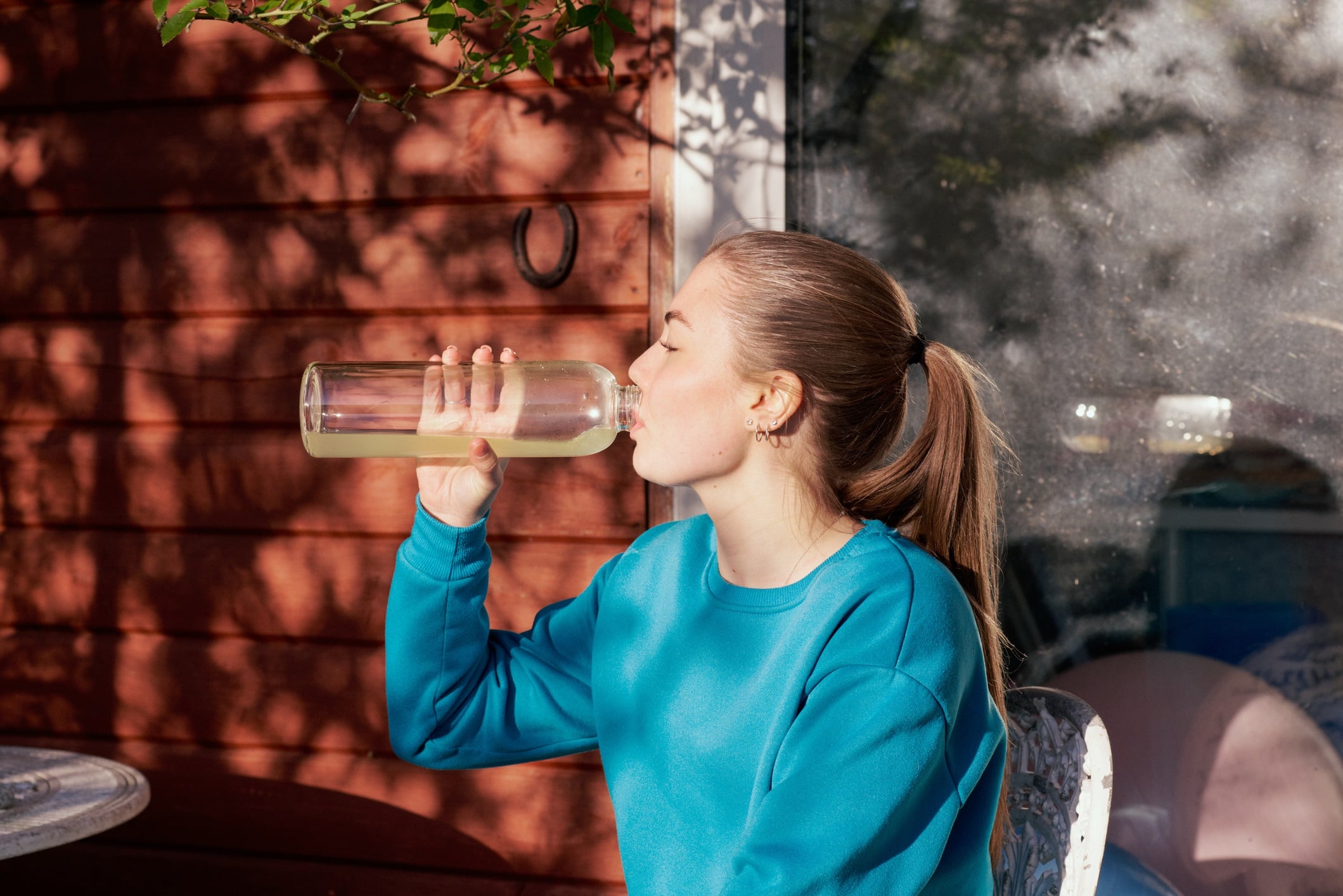 Woman wearing blue jumper sitting outside drinking from a reusable bottle.