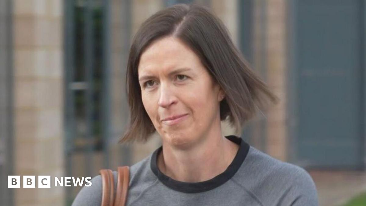Dr Kate Searle arrives for a hearing at a tribunal - she is wearing a grey top, has a brown handbag over their shoulder and has brunette hair