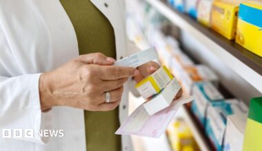 Close up of female pharmacist looking for medicines by the rack. Chemist searches the medicines on storage shelf, focus on hands holding medicine box.
