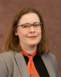 Headshot of woman with brown hair and glasses wearing an orange scarf