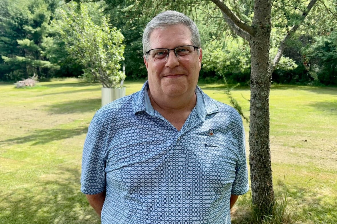 A man in a blue golf shirt standing outside on a sunny day.