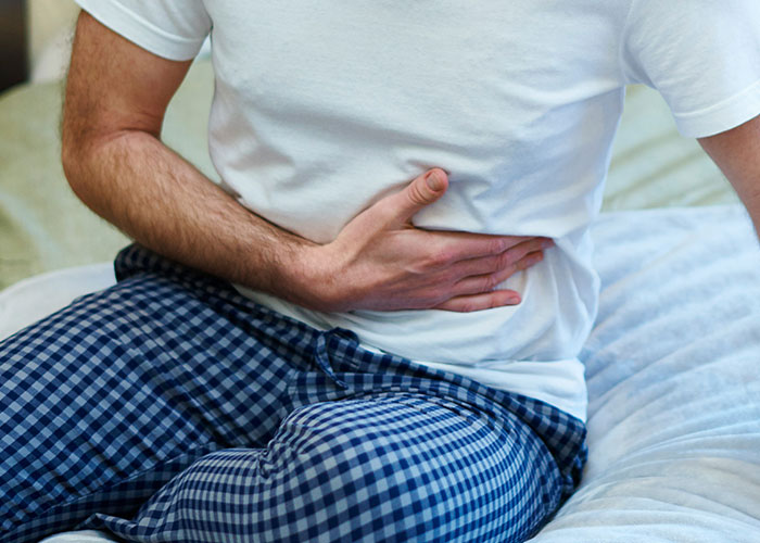 Man in pajamas holding stomach in pain on bed, illustrating patients delayed help with shocking consequences.