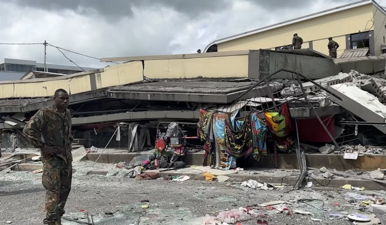 A soldier stands in front of a collapsed building.