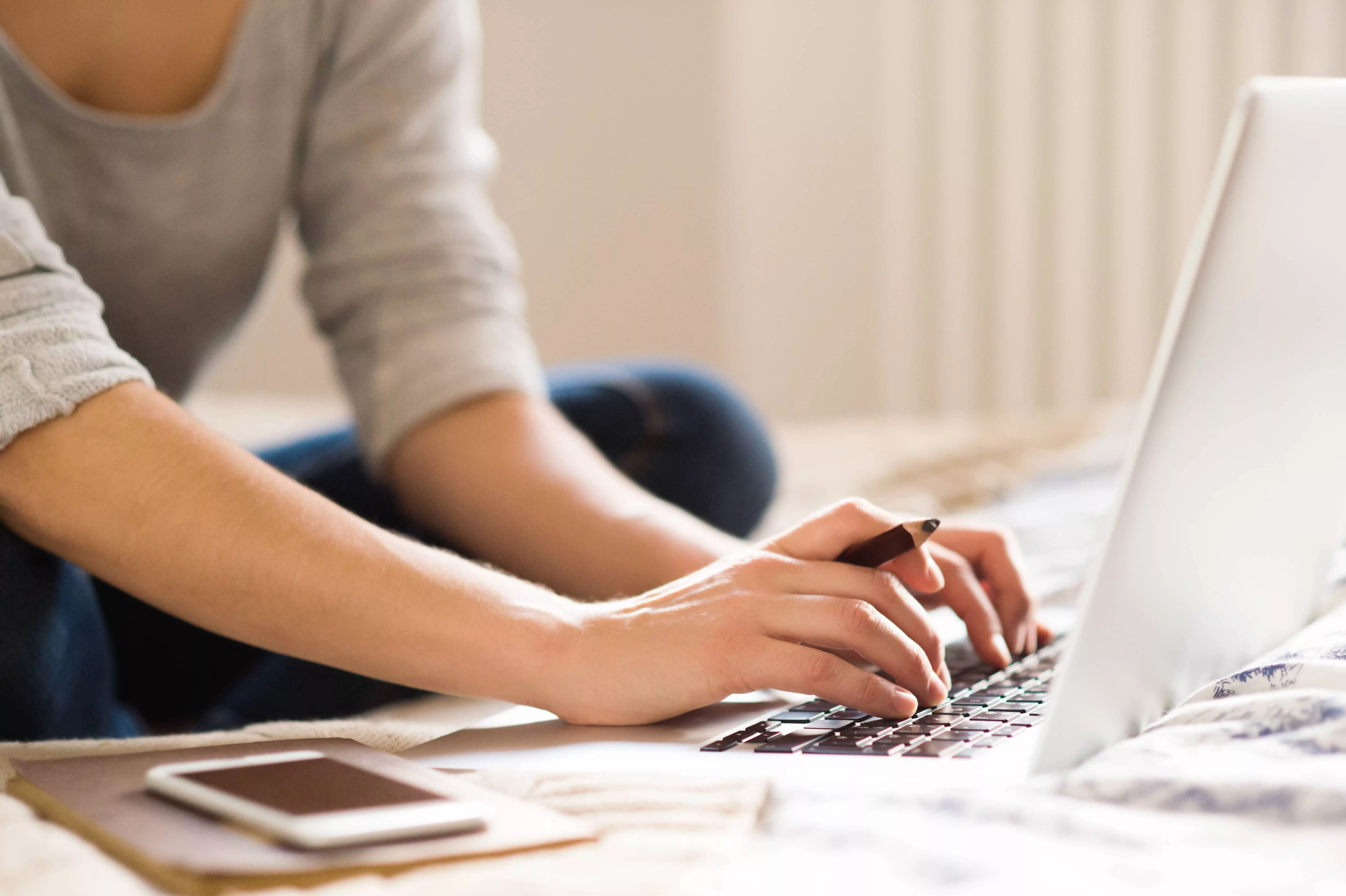 unrecognizable-young-woman-sitting-on-bed-working-home-office