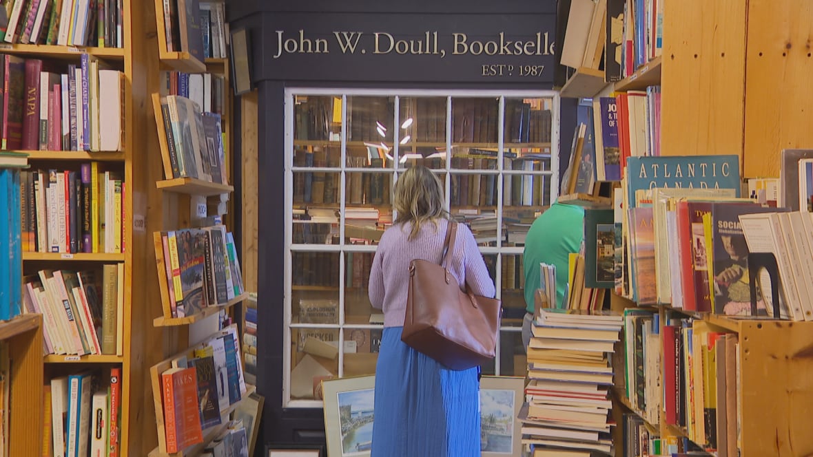 A woman stands in front of a sign reading John W. Doull, Bookseller. She is surrounded by books