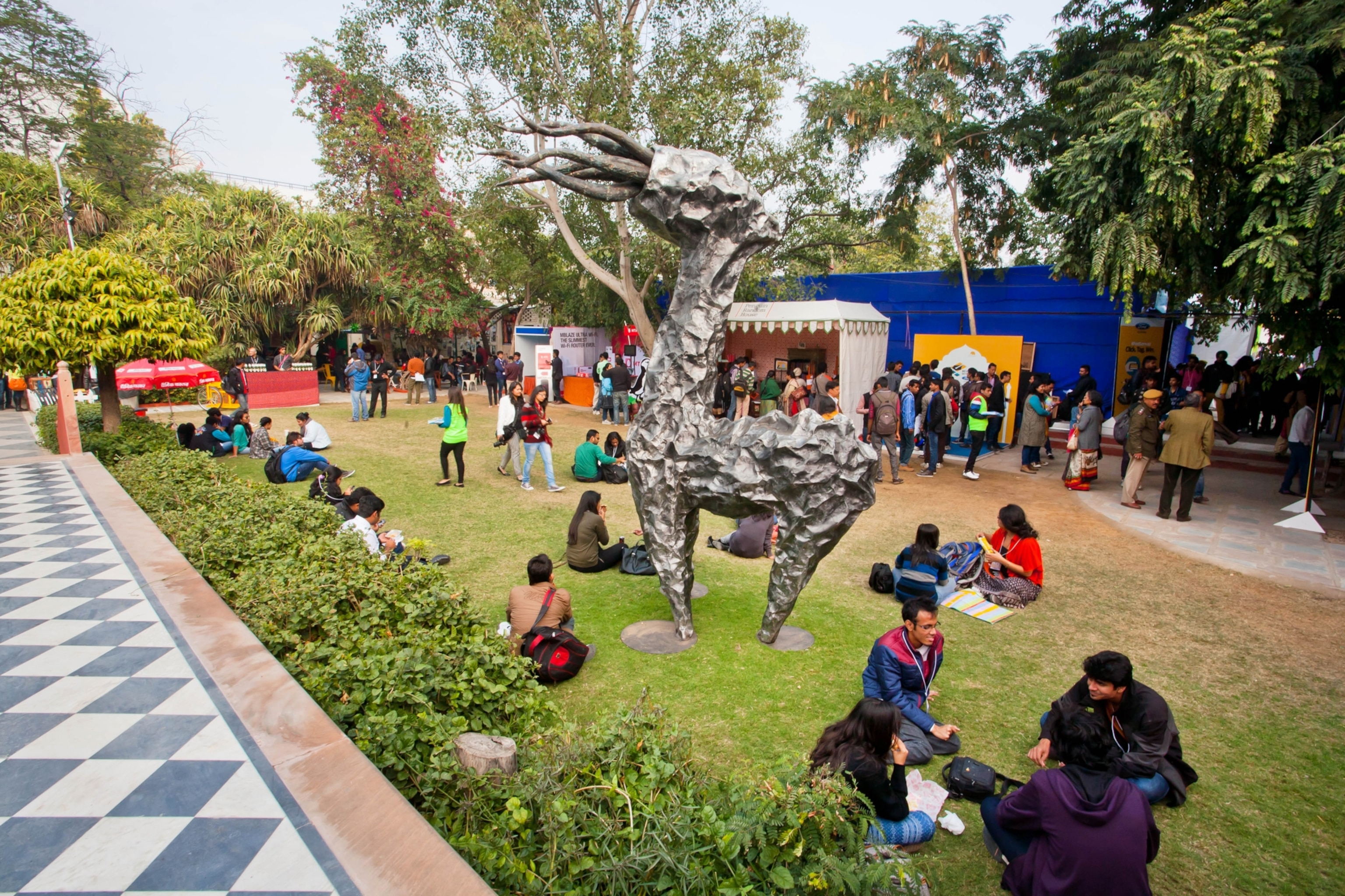 A group of people sit on a lawn with a sculpture on grass.