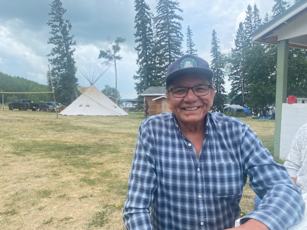 A man in glasses and a blue-checked shirt can be seen with a teepee behind him.
