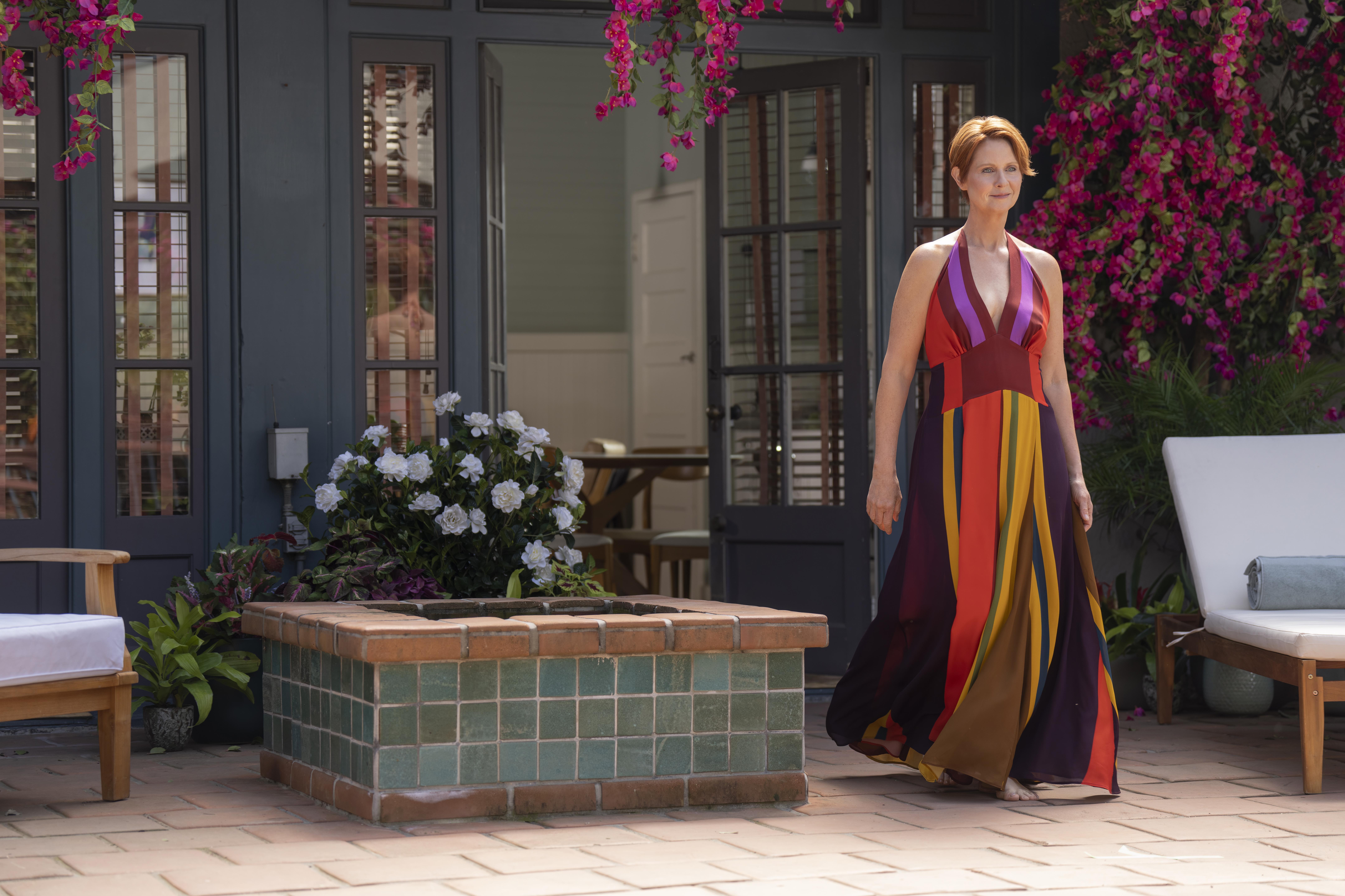 A woman in a colorful maxi dress walks barefoot across a patio.