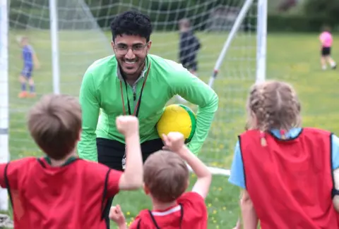 Getty Images A young male football coach talking to group of children in sports ground