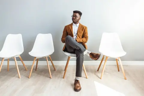 Getty Images Young man waiting for a job interview. He is neatly dressed in a jacket, trousers and smart shoes