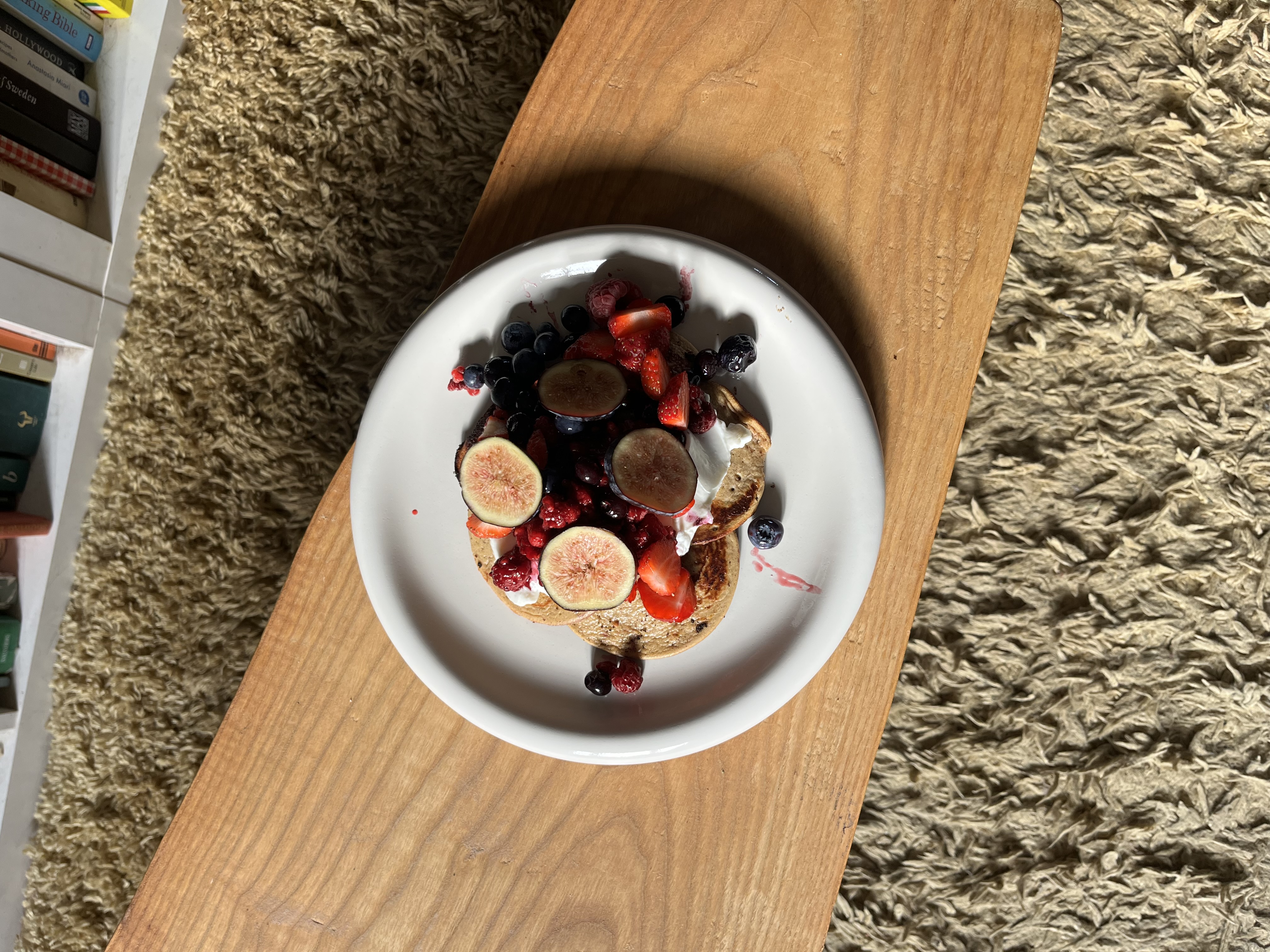 A plate of protein pancakes with fresh berries sitting on a wooden coffee table