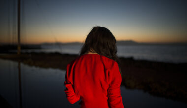 A woman in red looks out towards a dimming sunset.