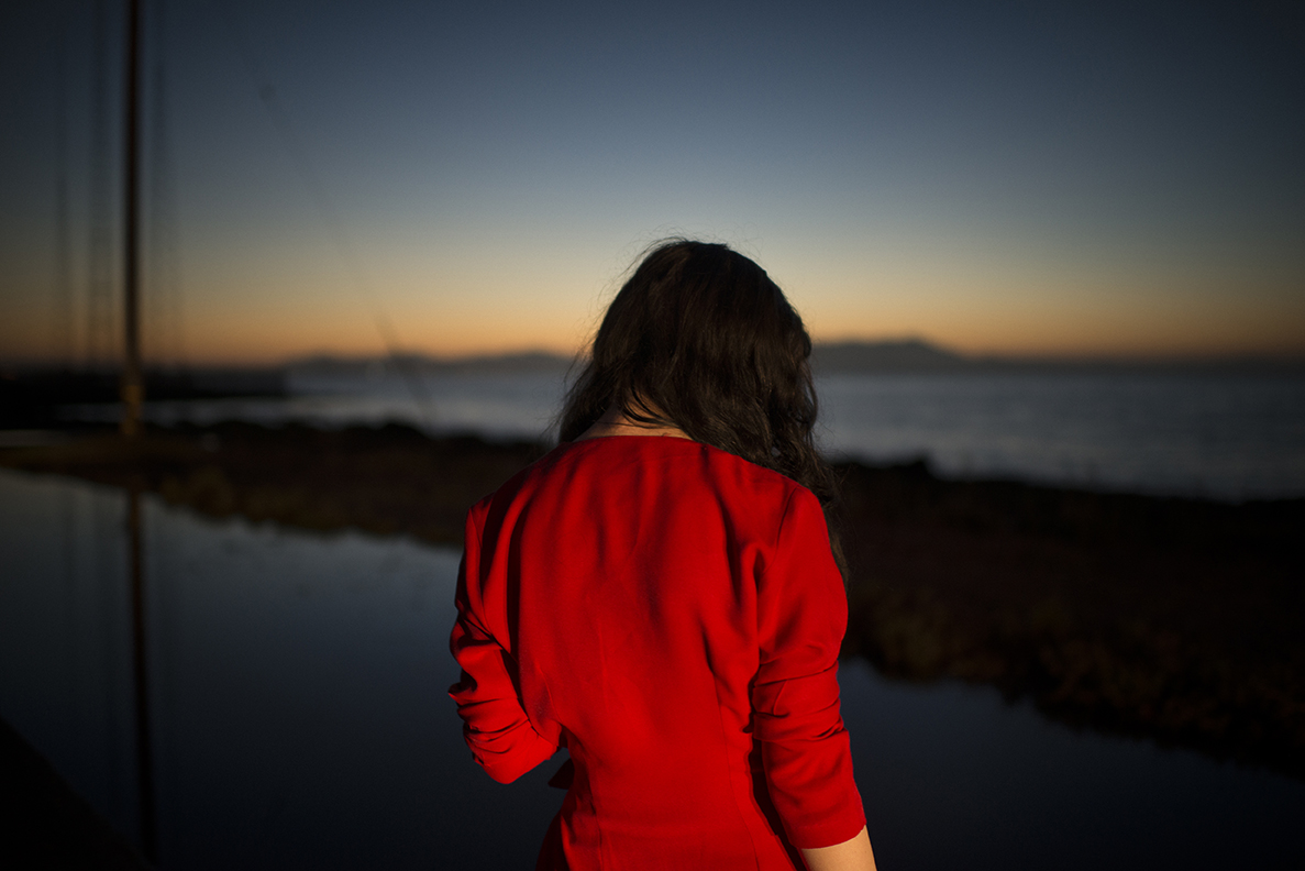 A woman in red looks out towards a dimming sunset.