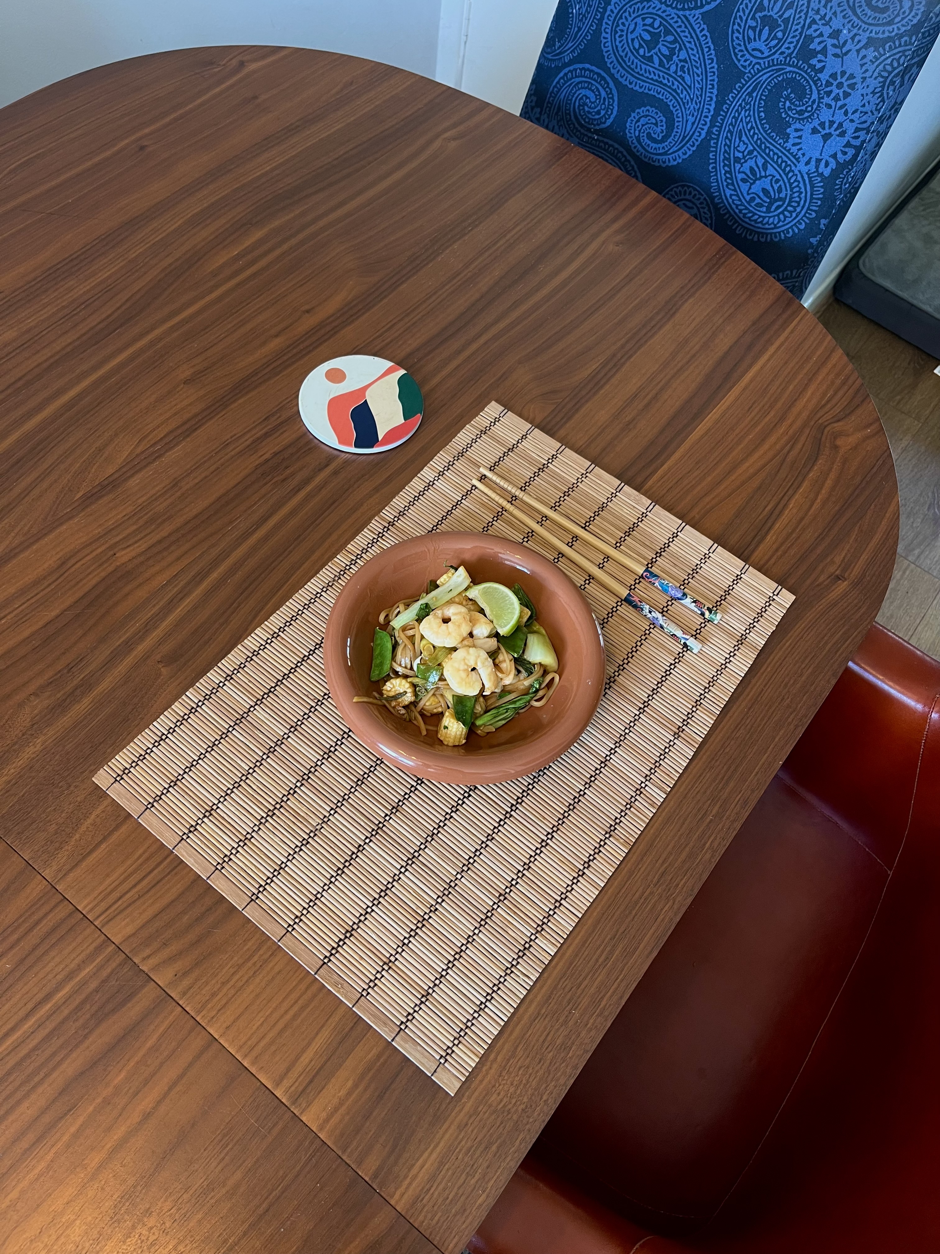 A bowl of chilli and garlic prawn noodles on a table with a set of chopsticks beside it