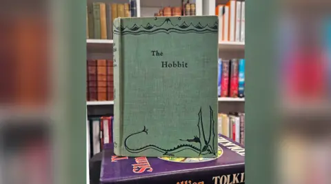 Auctioneum A copy of The Hobbit book. It is green with black text and an illustration at the bottom of the cover.