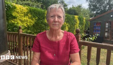 A woman in a dark pink top and grey hair sitting at a garden table
