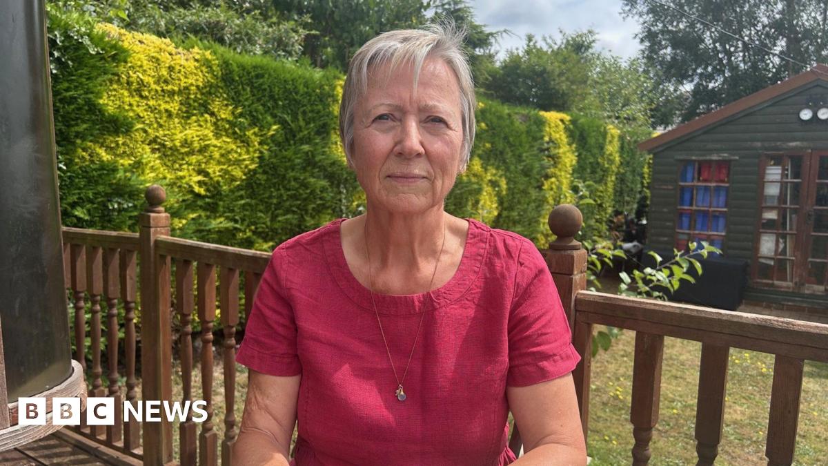 A woman in a dark pink top and grey hair sitting at a garden table