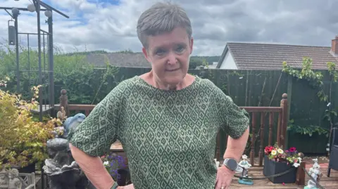 A woman in a green diamond patterned top standing on the decking of her garden