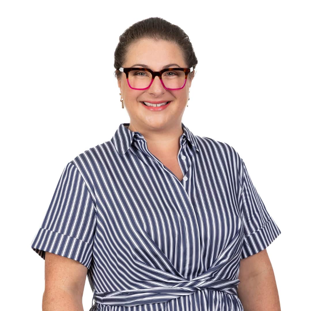 A woman smiles in a blue-and-white striped dress and glasses that are half tortoiseshell, half pink.