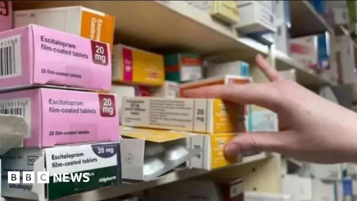 Boxes of medication on a shelf in a chemist, with a hand reaching for two boxes.
