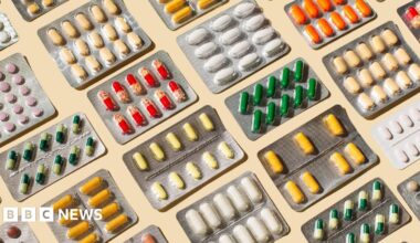 A stock image of many medications laid out in blister packs on a pale-coloured table.
