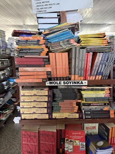 Piles of books differently stacked, all written by Wole Soyinka, rows of books in the background.