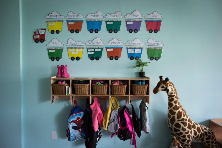 Cubby holes and coat hooks and a stuffed giraffe at the entrance of a daycare facility.
