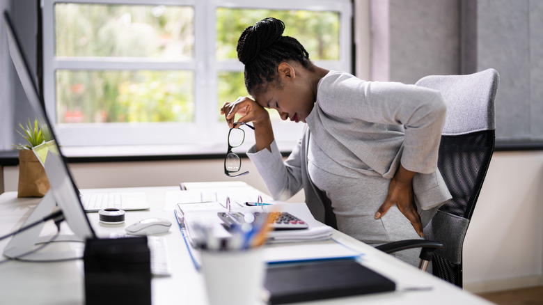 A woman at her desk holding her lower back in pain