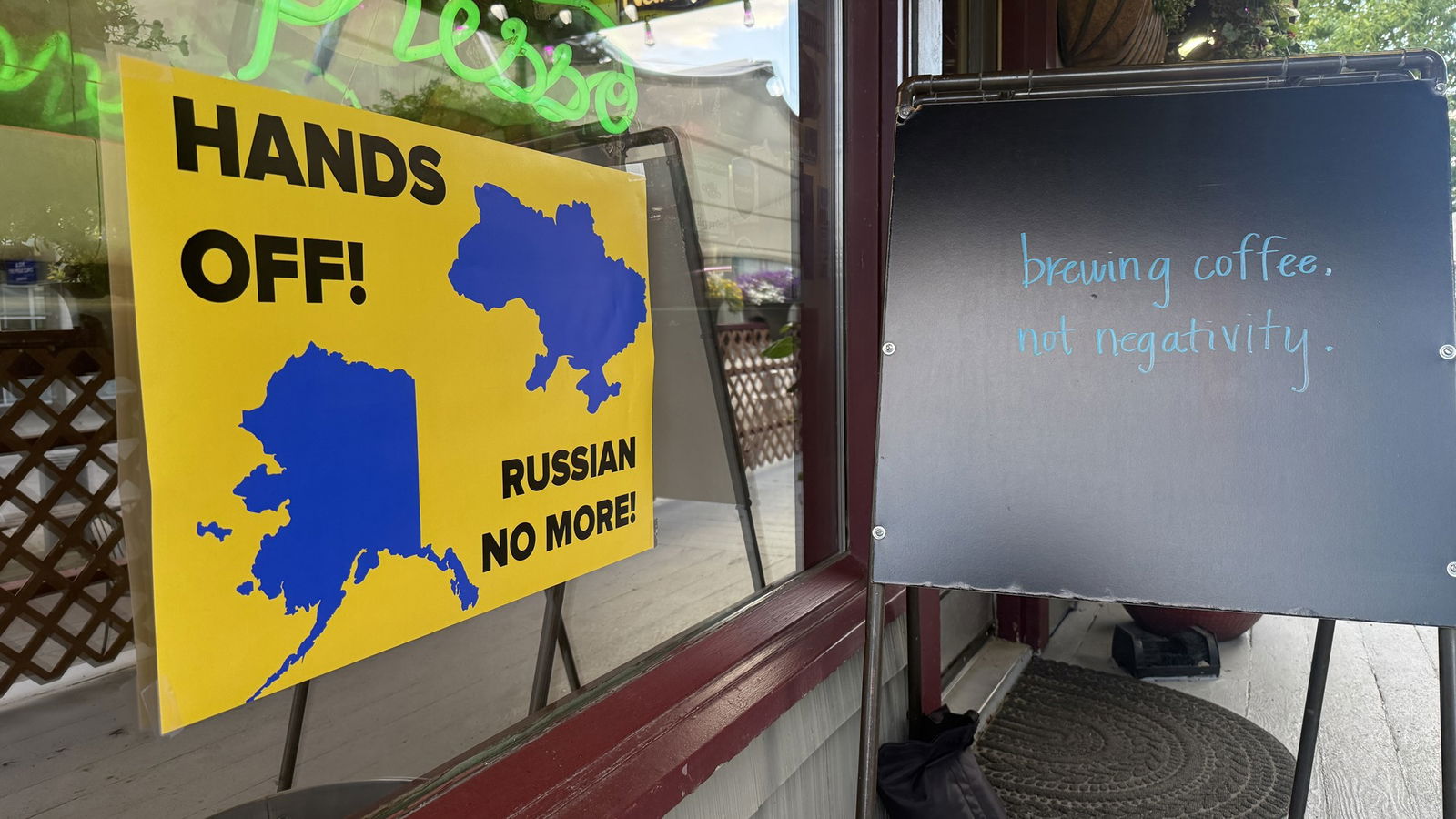 A sign says 'Hands off! Russian no more!' with silhouette maps of Ukraine and Alaska.