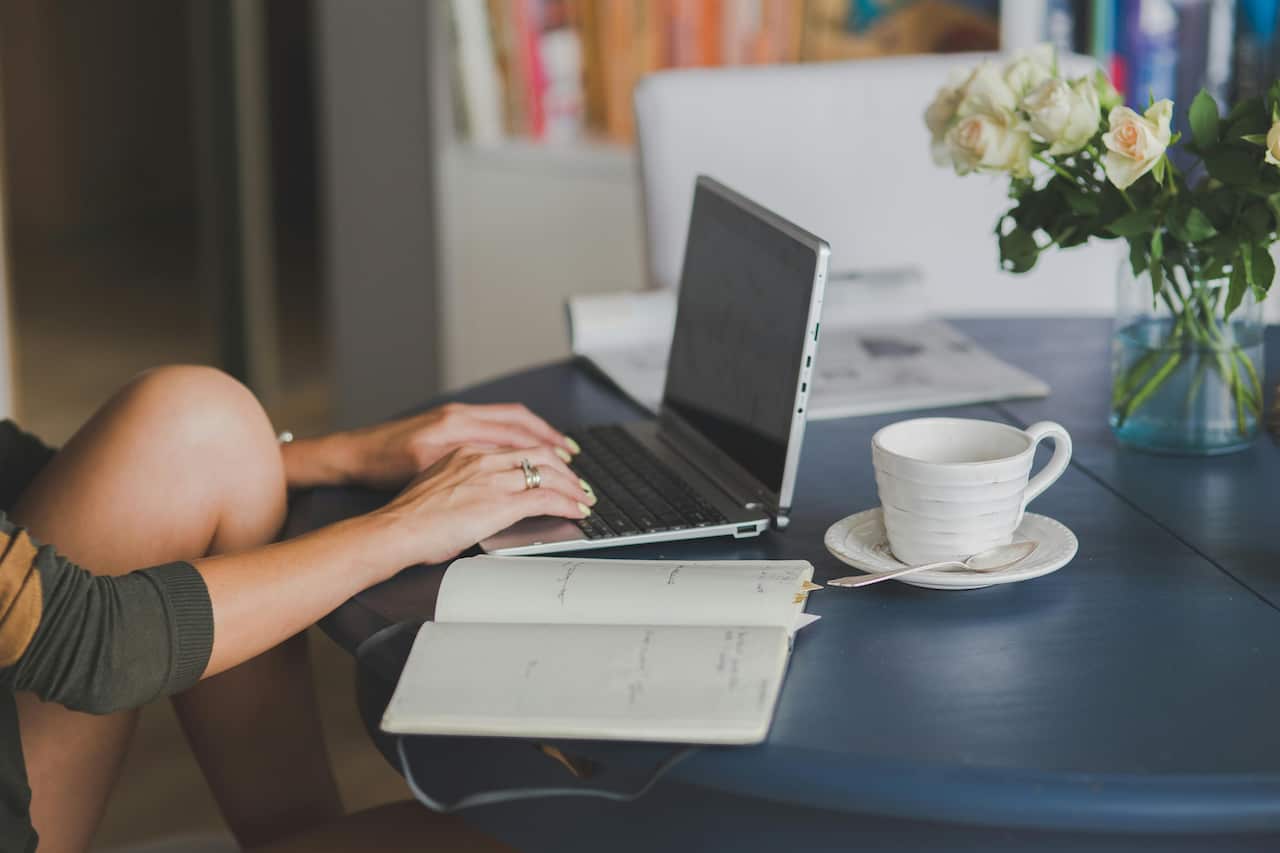 A person's hands on a laptop keyboard on a table. There is an open diary beside them
