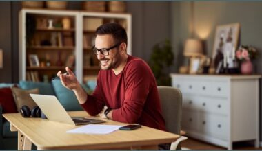 Man smiling, looking at a laptop screen, working from home.