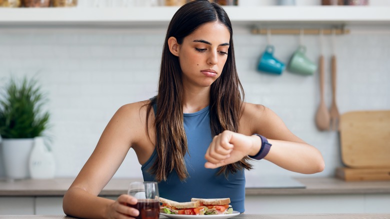 woman looking at her watch with plate of food on counter
