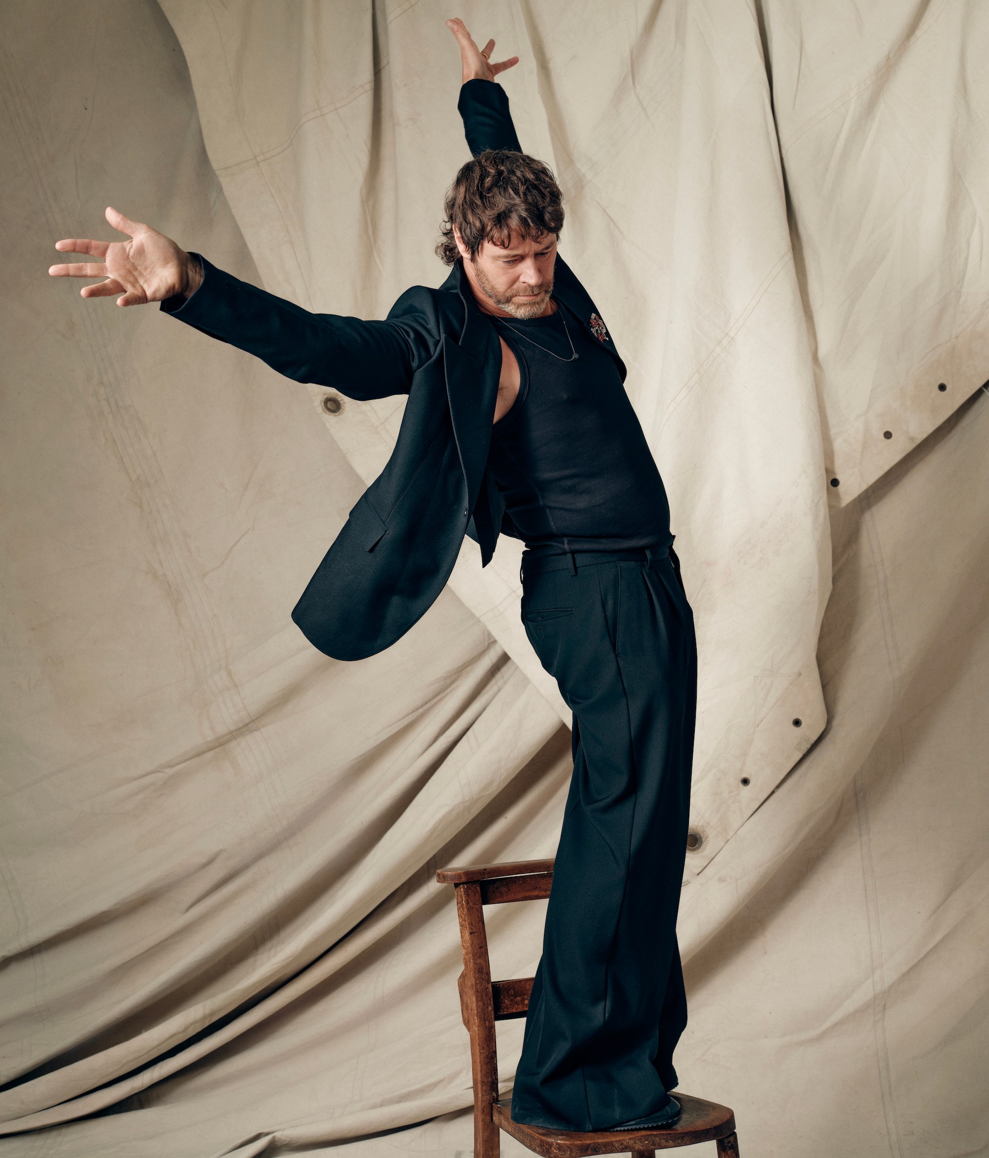 Portrait of a man in a black suit standing on a chair.