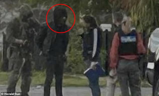 The man (pictured second from left) was arrested by heavily-armed officers on Friday