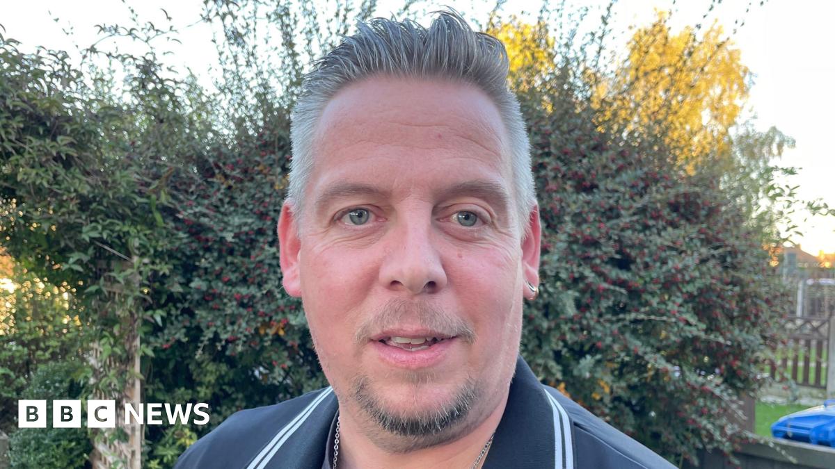 Man with goatee beard in dark shirt in front of a hedge