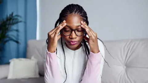 Getty Images A young woman is sitting on the sofa at home with her head in her hands