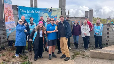 About a dozen volunteers are posing for a group photograph. One member is holding an award from the Marsh Volunteer Awards for Marine Conservation.