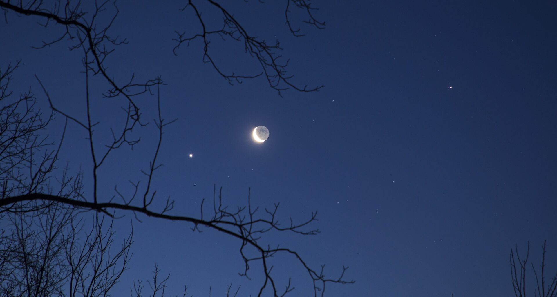 A photo of a crescent moon with brightly shining planets and stars