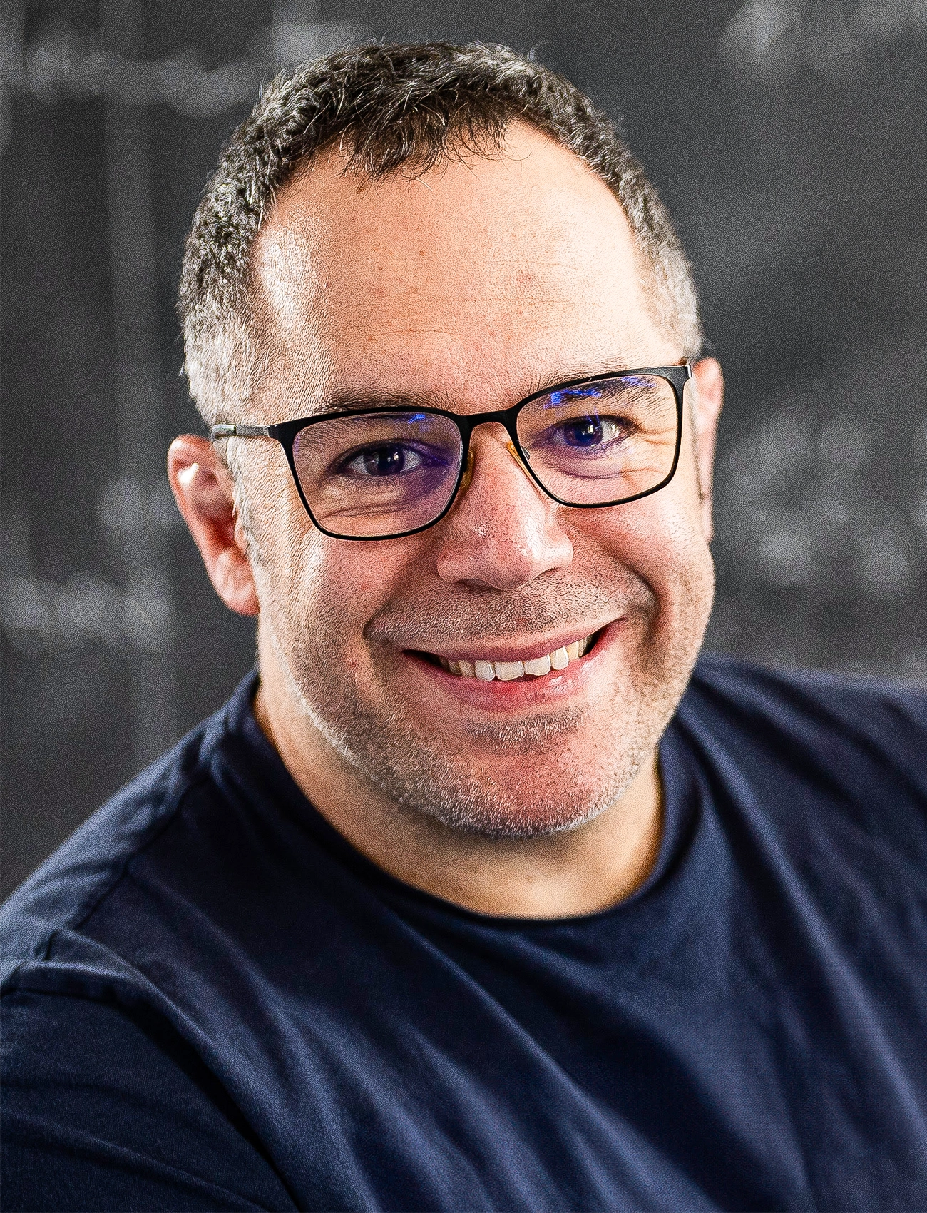 A man in glasses smiles at the camera.