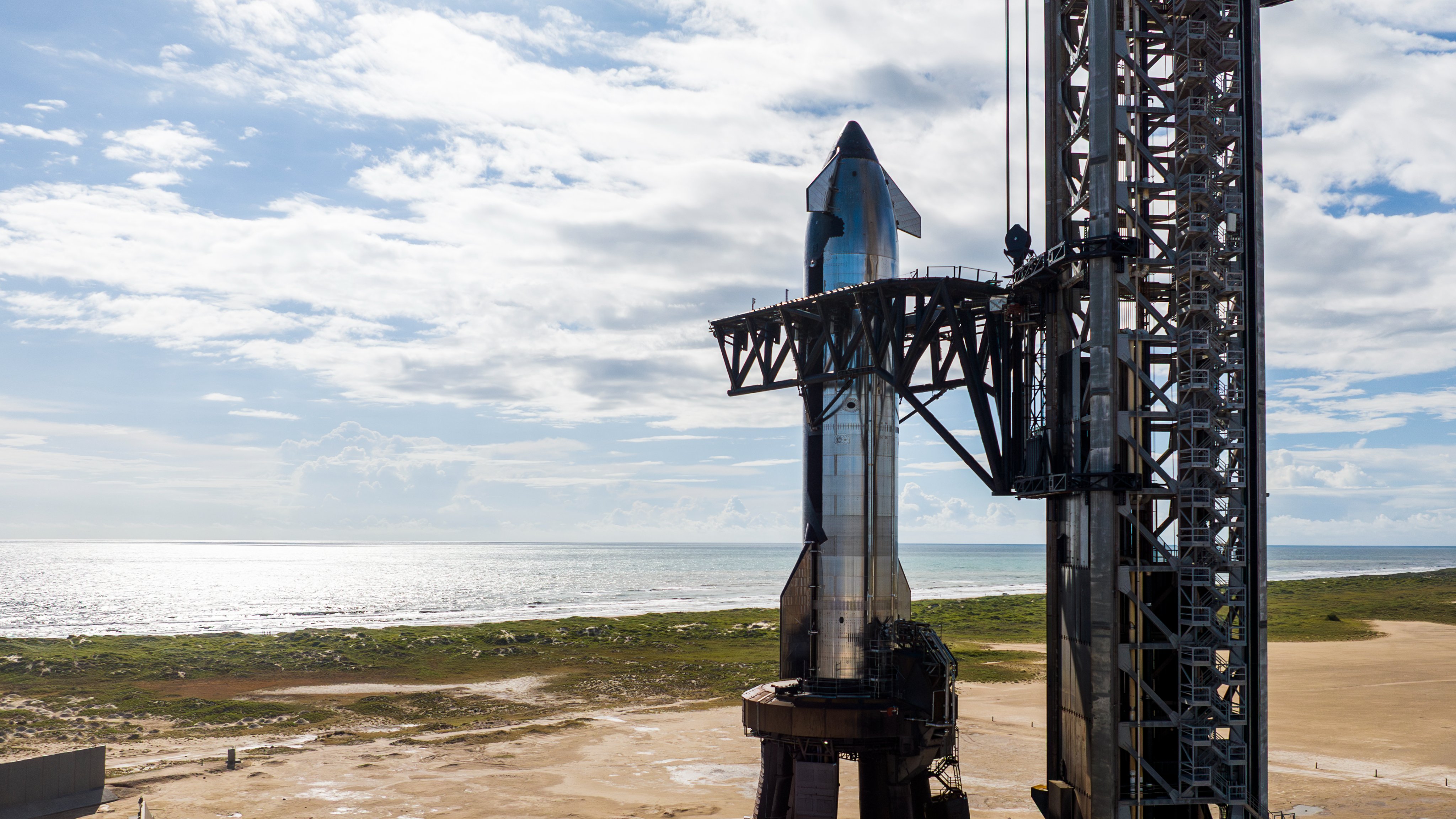 a shiny silver rocket sits at a seaside launch pad