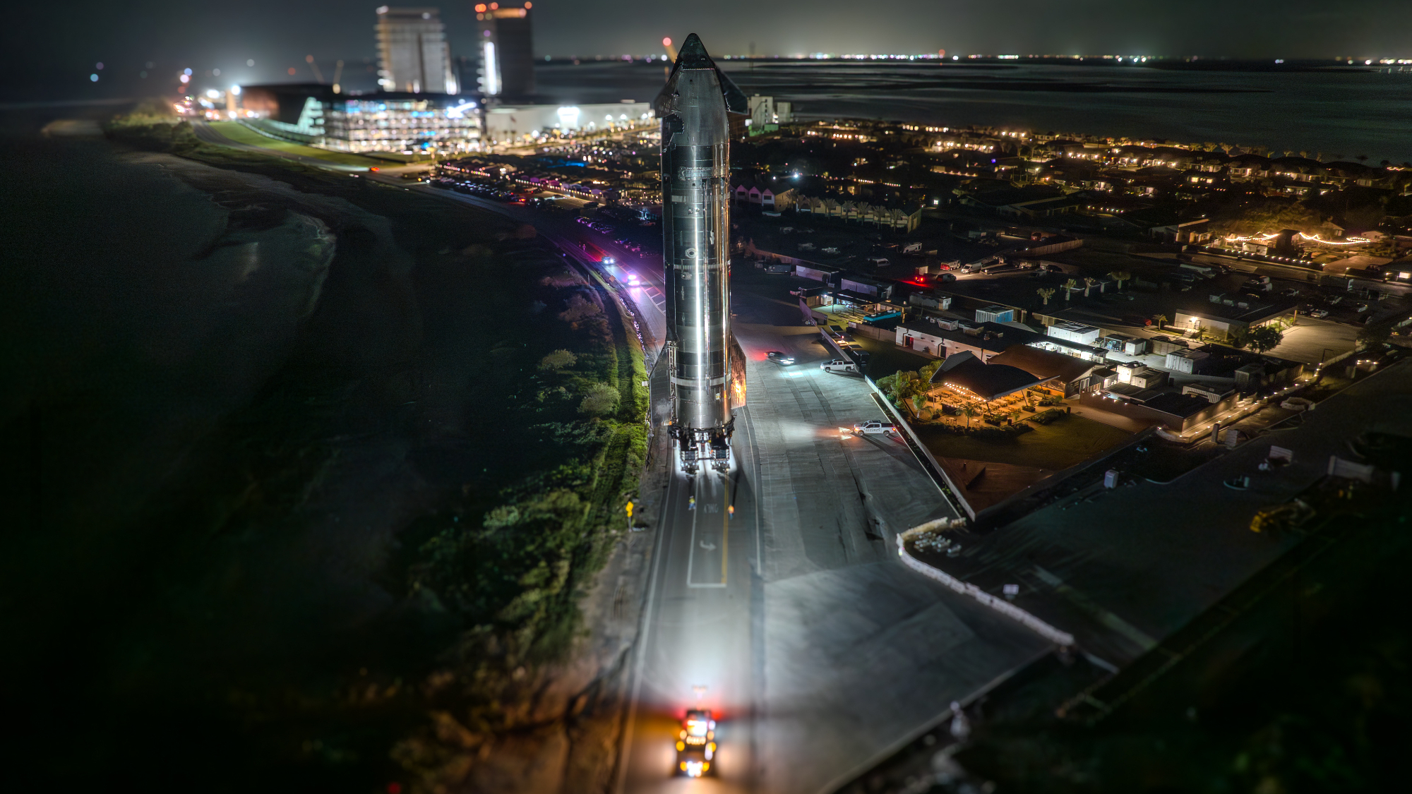 overhead photo of a large silver spacecraft rolling down a road at night