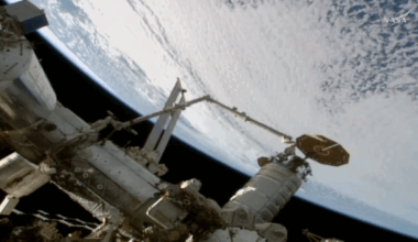 a spacecraft is held by a robot arm over Earth