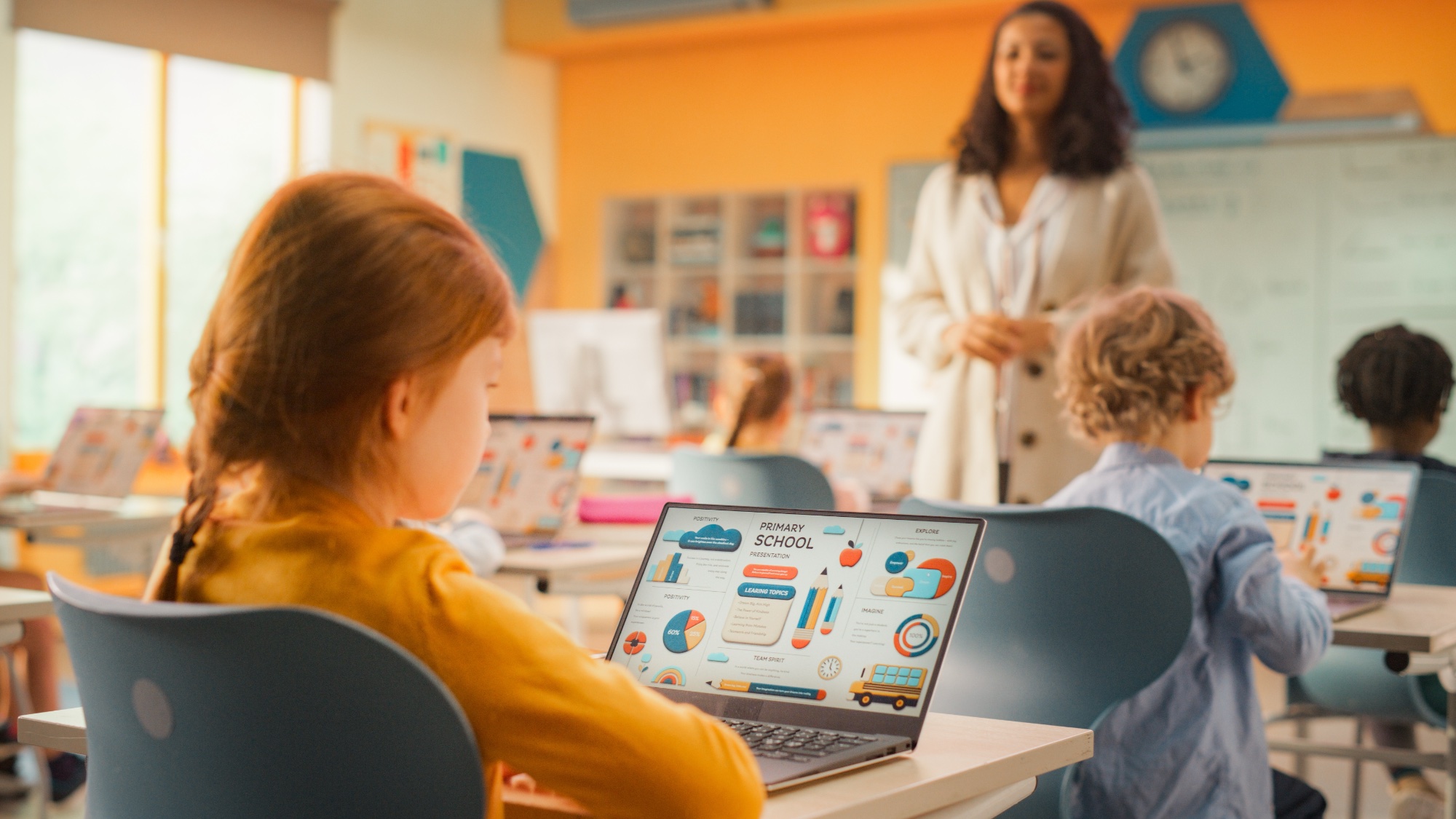 children in school on their laptops with teacher in front of class
