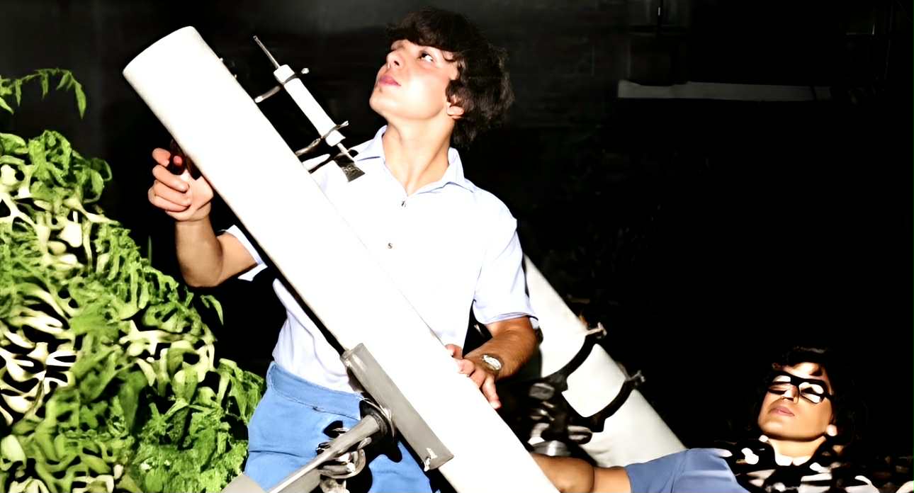 two men look up to the sky while operating a telescope