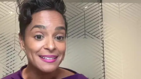 Jasmine smiles to camera - she is wearing a purple top. She is in an office. 