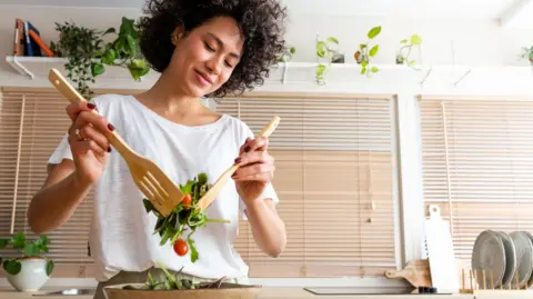 Getty Images Happy young woman mixing bowl of fresh salad.